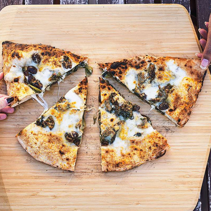 wo hands holding slices of cooked calzone with escarole and provola on top of an Ooni Bamboo Pizza Peel & Serving Board on a table.
