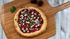 Pizza topped with beetroot and feta on top of a wooden pizza peel