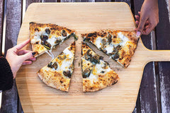 wo hands holding slices of cooked calzone with escarole and provola on top of an Ooni Bamboo Pizza Peel & Serving Board on a table.