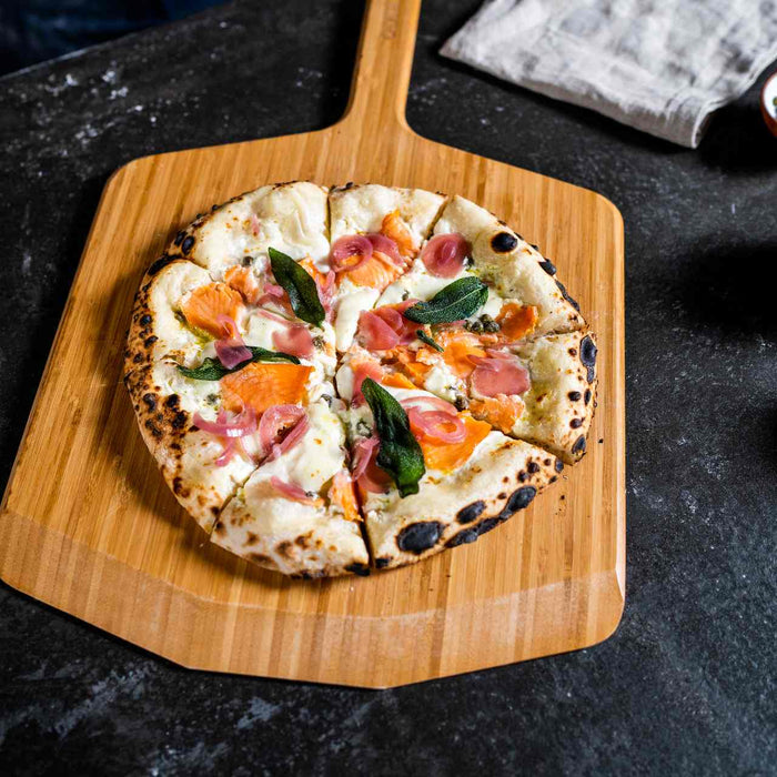 Finnish pizza with salmon, capers, pickeld onions, basil and crème fraîche on an Ooni Bamboo Pizza Peel.