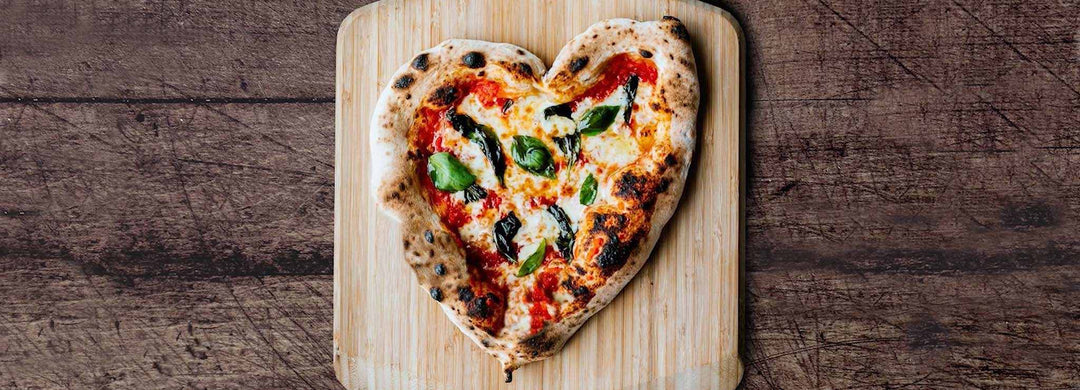 A heart shaped pizza topped with tomato, cheese and basil on a wooden pizza peel