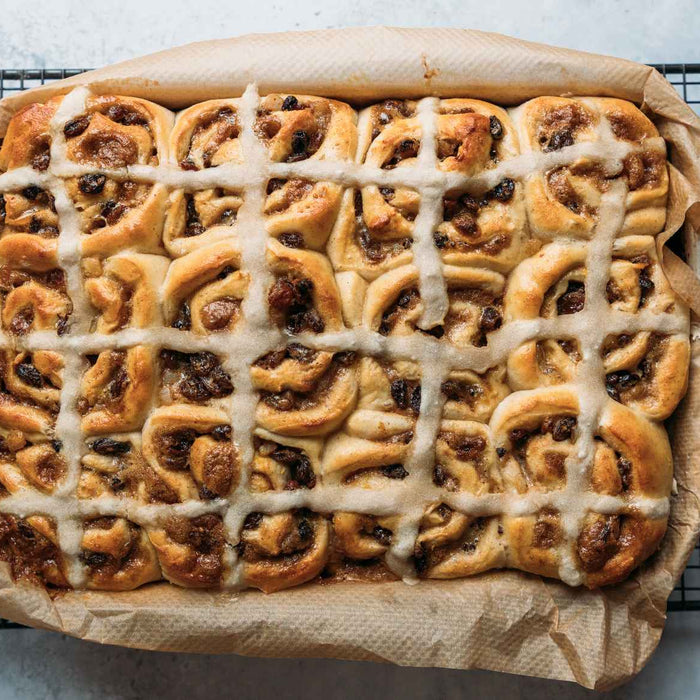 Hot cross Chelsea buns with an iced topping on a piece of parchment paper on a wire rack