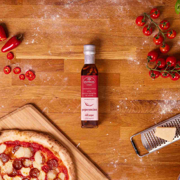 A wooden table top with tomatoes, chillies, garlic, parmesan, chilli oil and pizza showcasing the Ooni groceries range