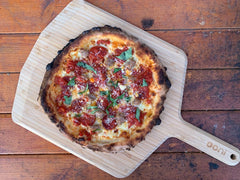 A thin crust pizza topped with tomato, cheese and basil on a wooden pizza peel. Baked using a Thin Crust Pizza Dough recipe.