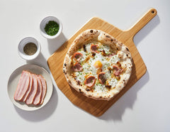 A wooden pizza peel with a pizza topped with cheese, egg and bacon