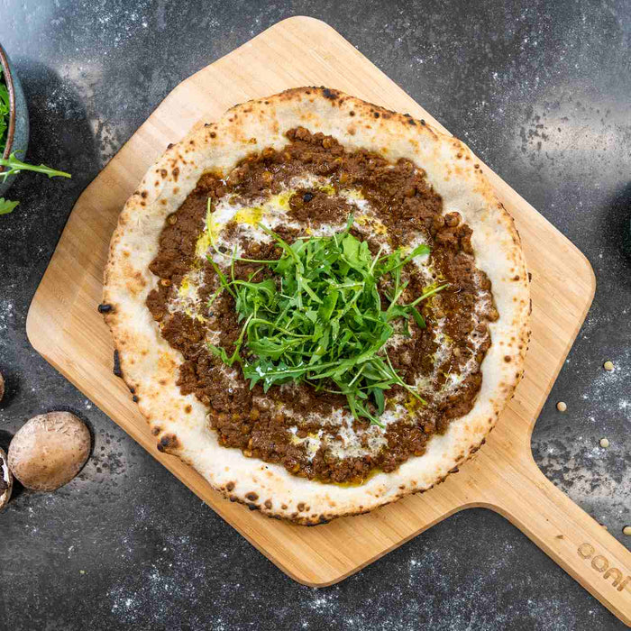 A pizza with mushroom ragu mince and rocket on top on a wooden pizza peel
