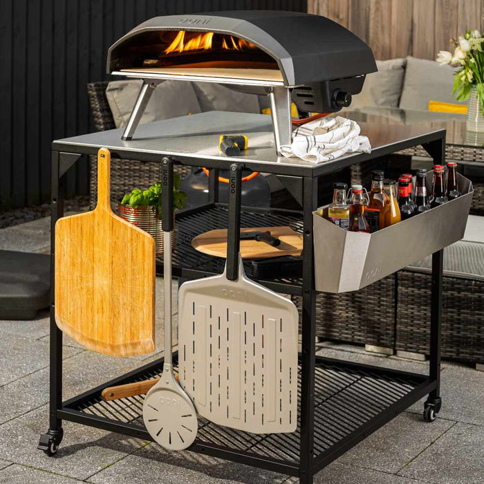 Ooni pizza oven on top of an Ooni modular table with a selection of pizza peels attached and hanging on hooks