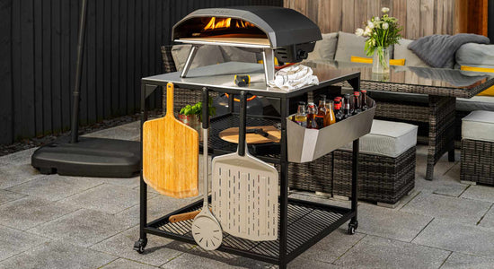 Ooni pizza oven on top of an Ooni modular table with a selection of pizza peels attached and hanging on hooks