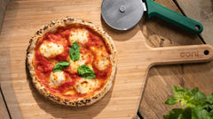 A pizza covered in cheese, tomato and basil on a wooden pizza peel baked using a Gluten-Free Pizza Dough recipe