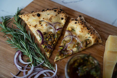 Two slices of pizza topped with pistachios and red onion on a wooden pizza peel with fresh rosemary