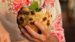 Hand holding a cooked pizzette stuffed with baby peppers, mozzarella, red chicory and basil.
