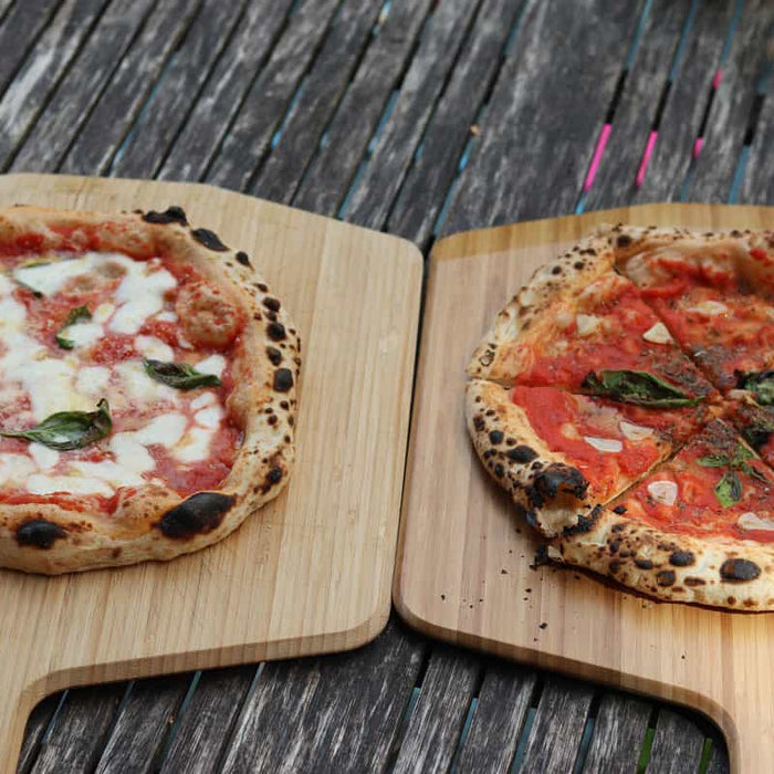 Two pizzas on wooden pizza peels baked using a 100% Biga pizza dough recipe