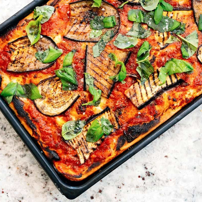 Pizza topped with tomato, aubergine and fresh basil in a metal sheet pan. Baked using a Sicilian pizza recipe.