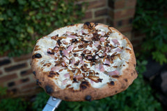 Cooked Alsatian tarte pizza with crème fraîche, fromage frais, white onion, bacon and shallots on an Ooni Pizza Peel.