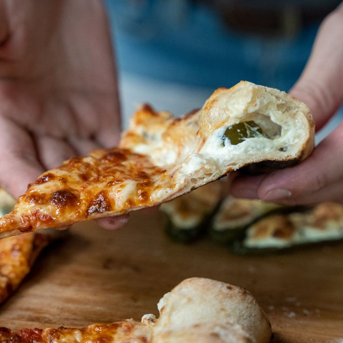 A slice of pizza with a jalapeno stuffed crust being held over a wooden pizza peel