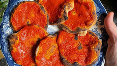 Hand holding a plate with six cooked pizzette rosse with tomato sauce.