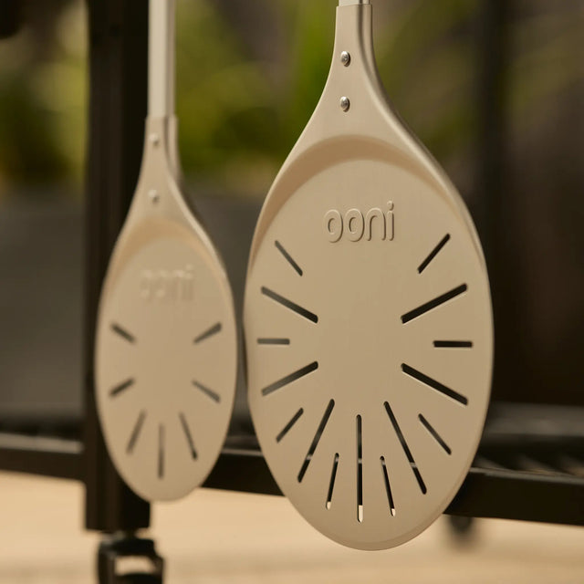 side by side of compact and wide pizza turning peel hanging from modular table. 