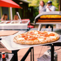 Ooni Pizza Peel with cooked pepperoni on top with Koda Oven in the background