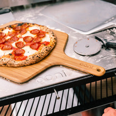 Ooni Bamboo peel with pizza on top with cutter wheel next to it