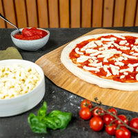 Raw pizza dough with sauce and cheese on top of a bamboo peel